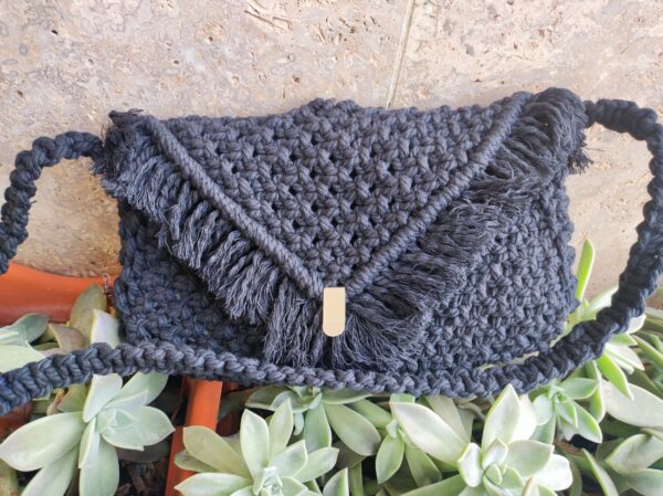 Bolso negro de macramé sobre superficie con plantas.